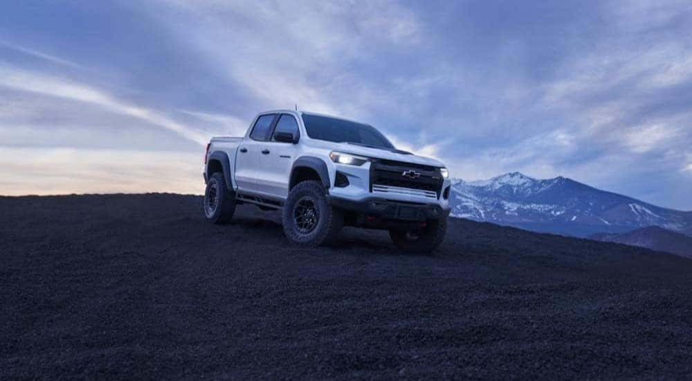 A white 2024 Chevy Colorado ZR2 Bison is shown parked off-road near mountains.