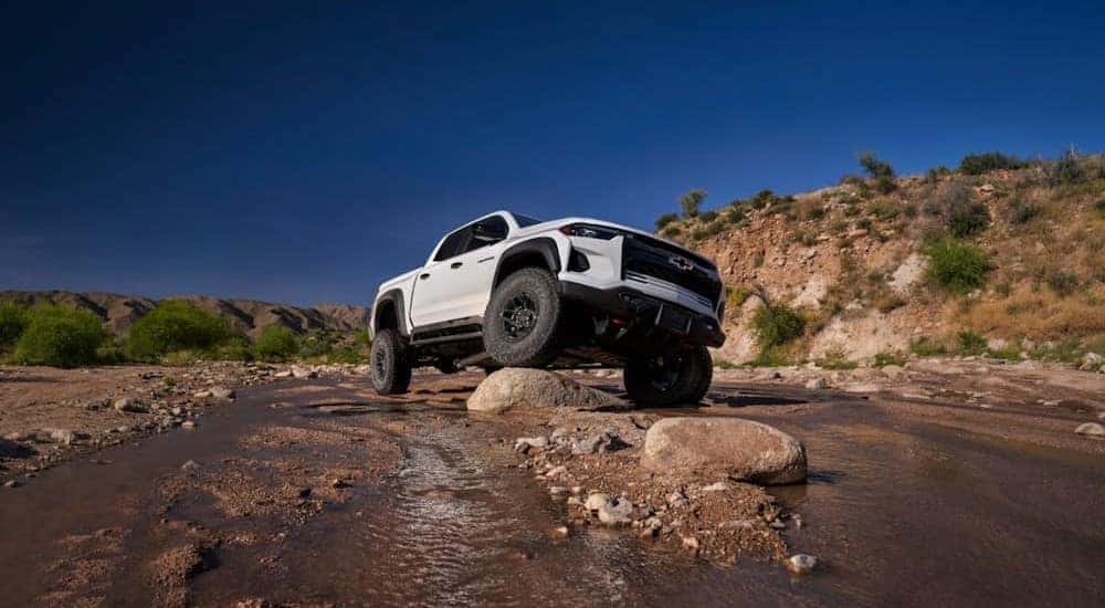 One of many popular Chevy trucks for sale, a white 2024 Chevy Colorado ZR2 Bison, is shown parked on a boulder off-road.