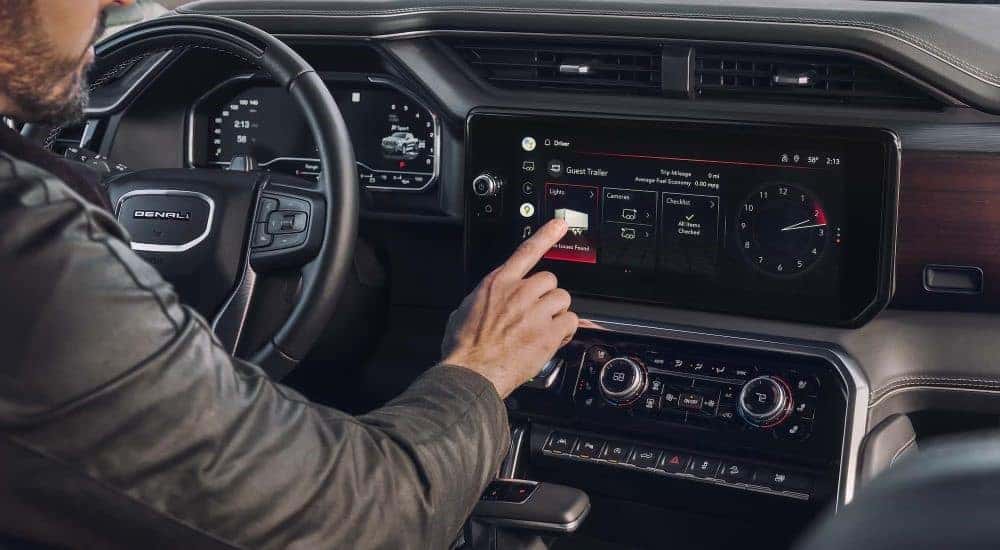A person is shown using the infotainment screen in a 2023 GMC Sierra 1500 Denali.