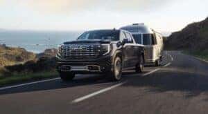 A black 2022 GMC Sierra 1500 Denali Ultimate is shown towing a silver camper on an open road.
