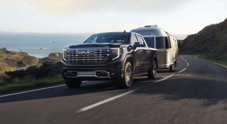 A black 2022 GMC Sierra 1500 Denali Ultimate is shown towing a silver camper on an open road.