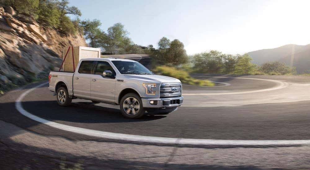 A white 2015 Ford F-150 is shown driving on a highway after viewing used for trucks.