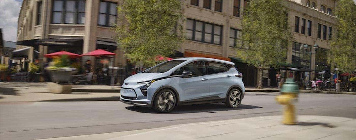 A blue 2023 Chevy Bolt EV is shown from the side on a city street.