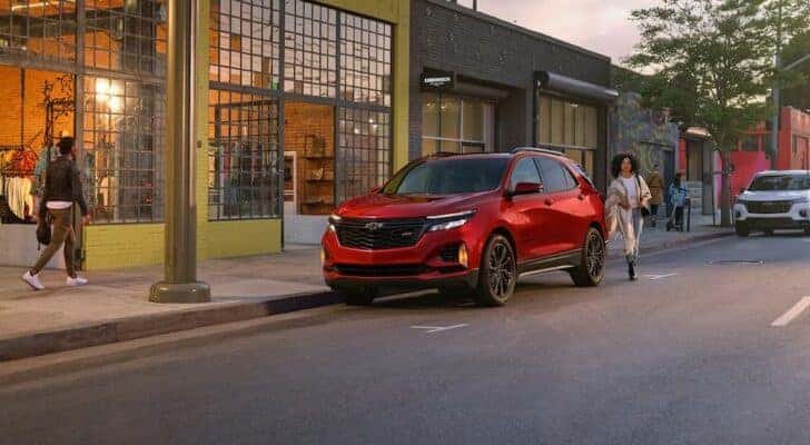 A red 2024 Chevy Equinox RS is shown parked on the side of a street near a store.