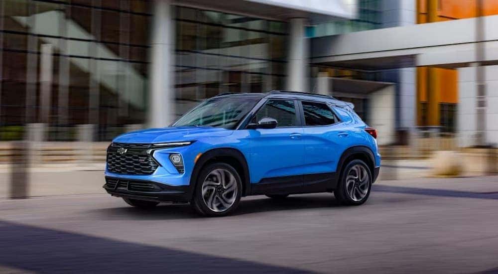 A new Chevy Trailblazer for sale, a blue 2024 Chevy Trailblazer EXT, is shown driving near a building.