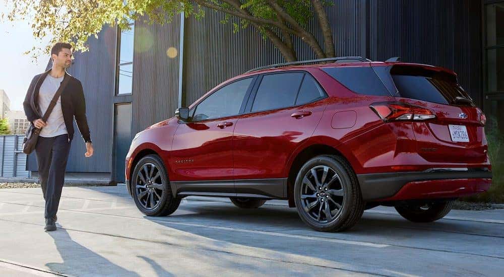 A man is shown walking from a red 2024 Chevy Equinox parked beside a curb.