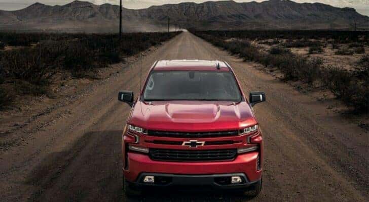 A red 2023 Chevy Silverado 1500 RST is shown from a front angle driving from a dealer with a Chevy Silverado for sale near Alpine, UT.