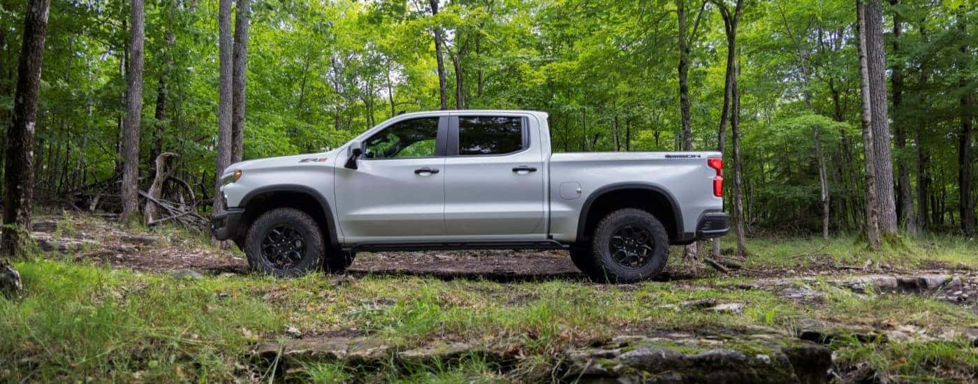 A white 2023 Chevy Silverado ZR2 Bison is shown from the side while parked off-road in a forest.