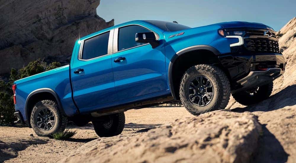 A blue 2024 Chevy Silverado 1500 ZR2 is shown driving up a rocky incline after visiting a dealer with a Chevy Silverado for sale near Alpine, UT.