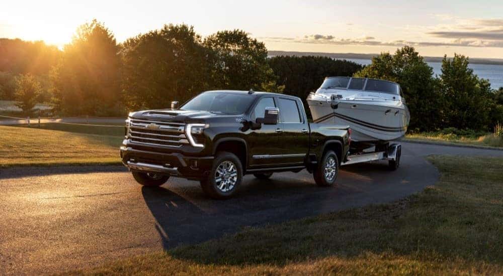 A black 2024 Chevy Silverado 2500HD High Country is shown towing a boat.