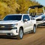 A white 2024 Chevy Silverado 1500 is shown towing a boat after visiting a dealer with a Chevy Silverado for sale near Kearns.
