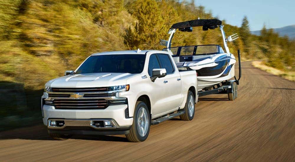 A white 2024 Chevy Silverado 1500 High Country is shown towing a boat after visiting a dealer with a Chevy Silverado for sale near Kearns.
