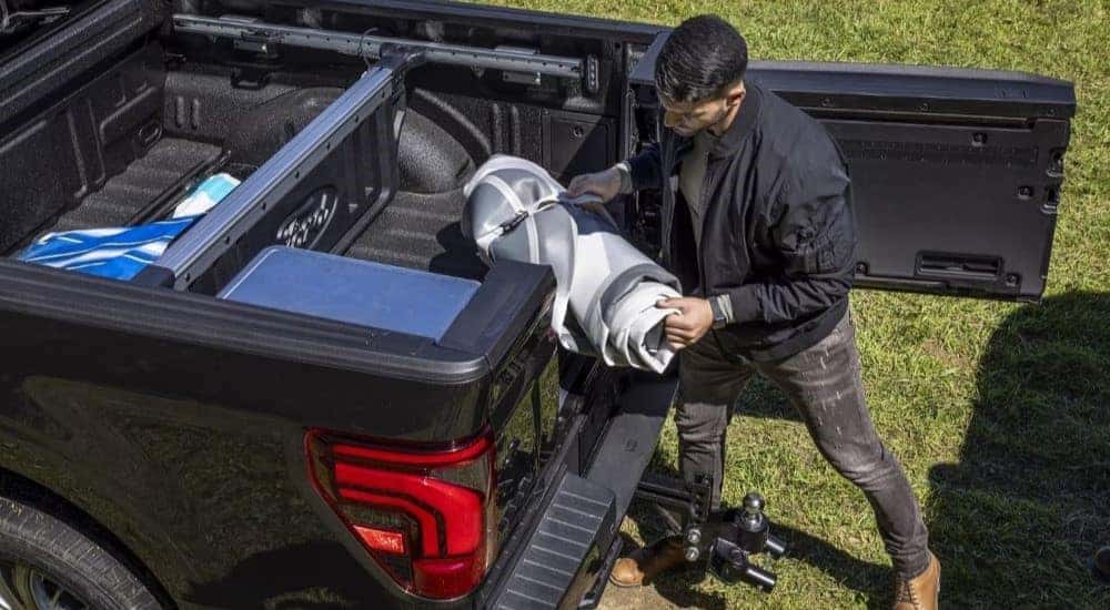 A person is shown loading equipment into the back of a black 2024 Ford F-150.