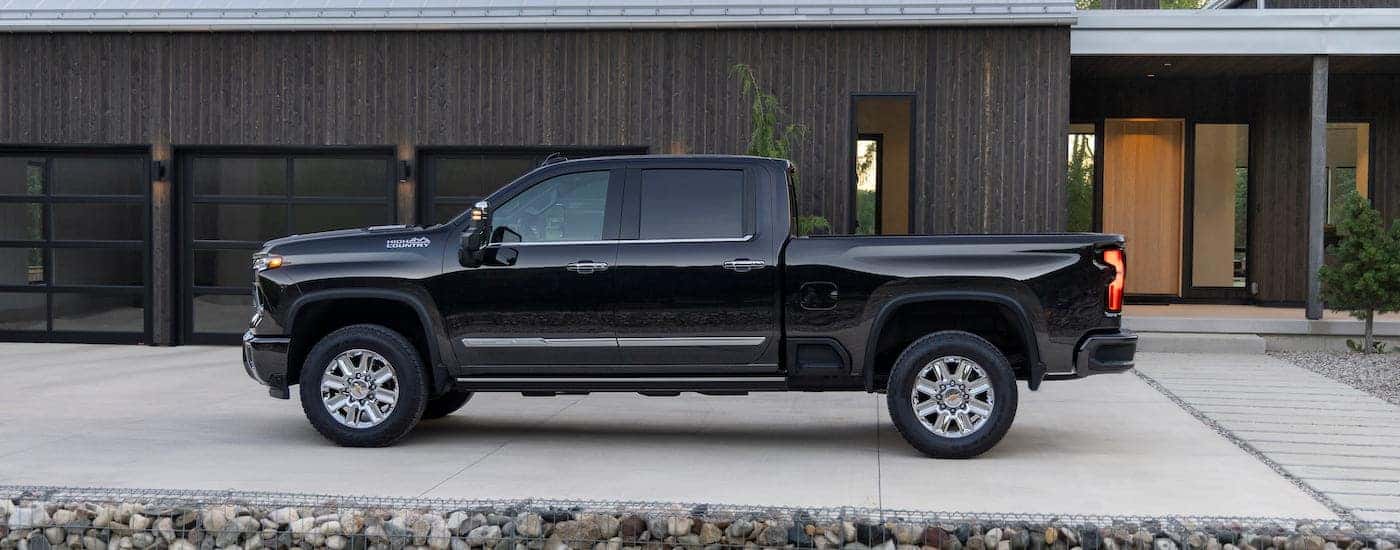 A black 2024 Chevy Silverado 2500 HD High Country is shown from the side while parked on a driveway.