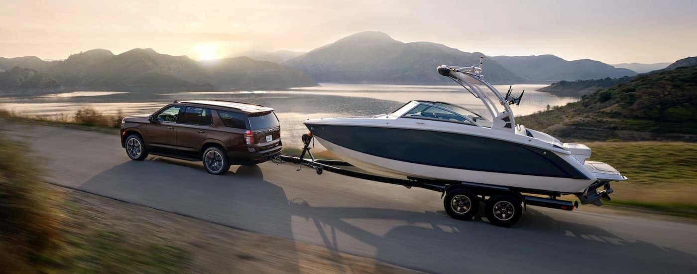 A brown 2023 Chevy Tahoe RST towing a boat on an open road.