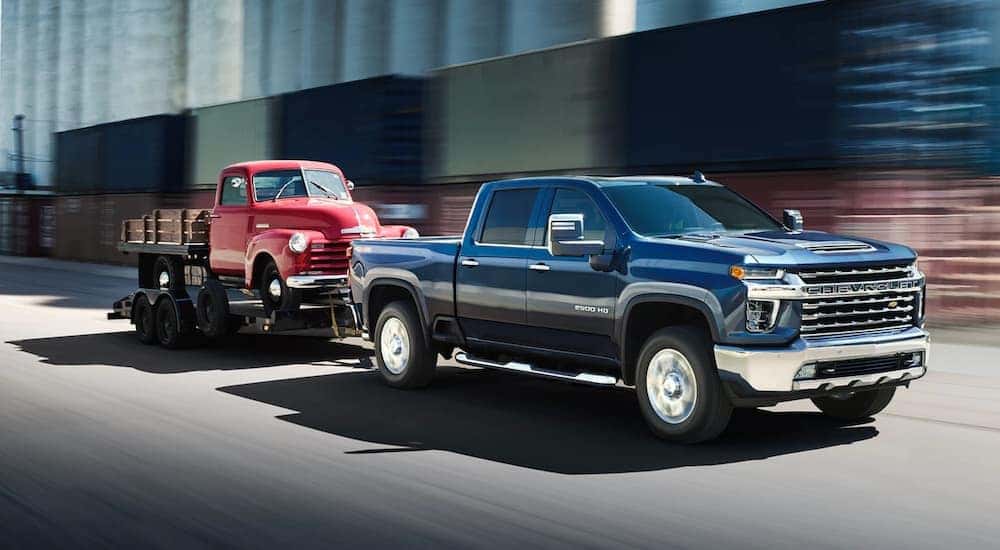 A blue 2020 Chevy Silverado 2500 HD is shown towing a red truck on a trailer.
