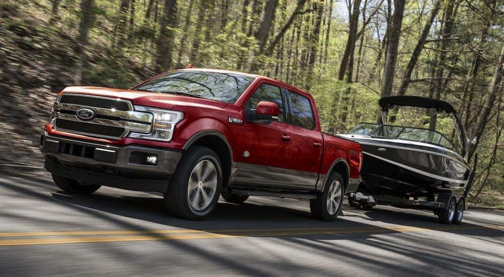 A red 2021 Ford F-150 is shown towing a boat after viewing used trucks for sale near Salt Lake City.