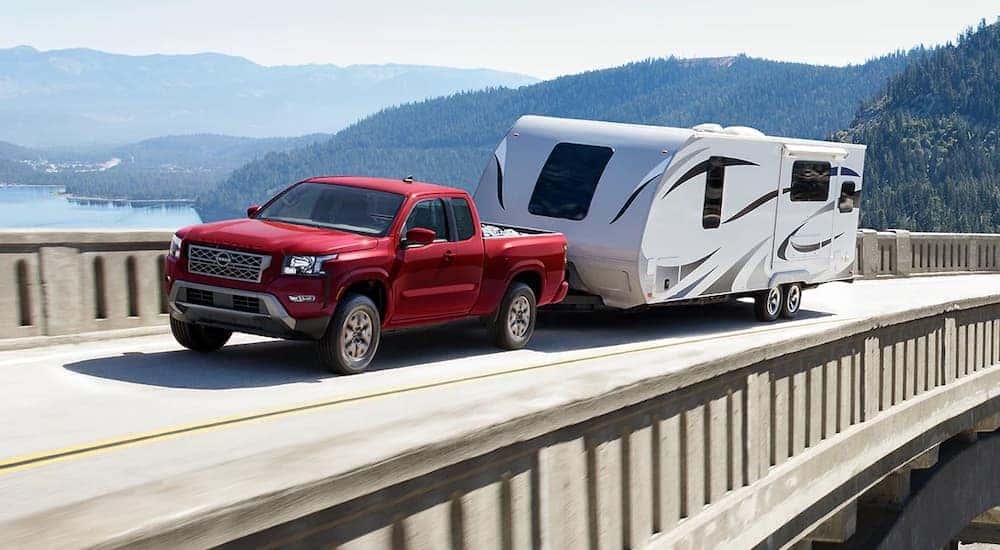 A red 2023 Nissan Frontier is shown towing a camper.