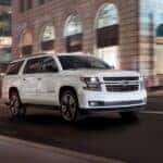 A white 2019 Chevy Suburban for sale is shown driving on a city street.