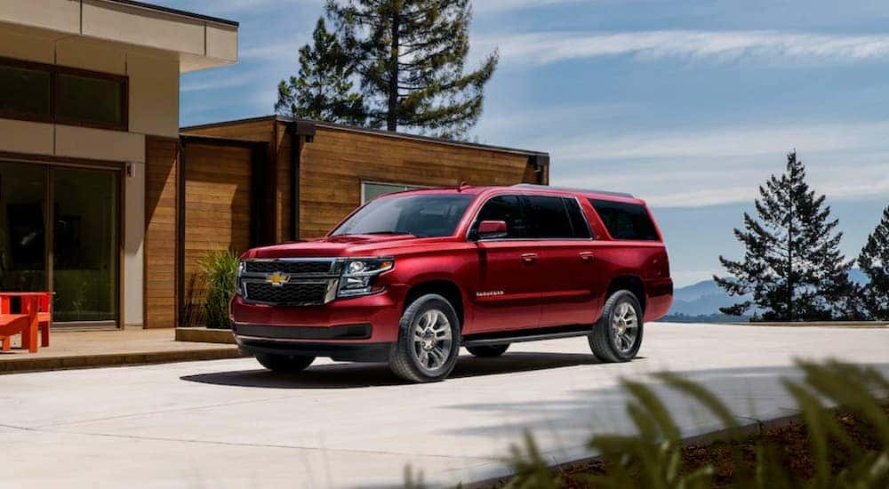 A red 2020 Chevy Suburban LT is shown parked near a modern home.