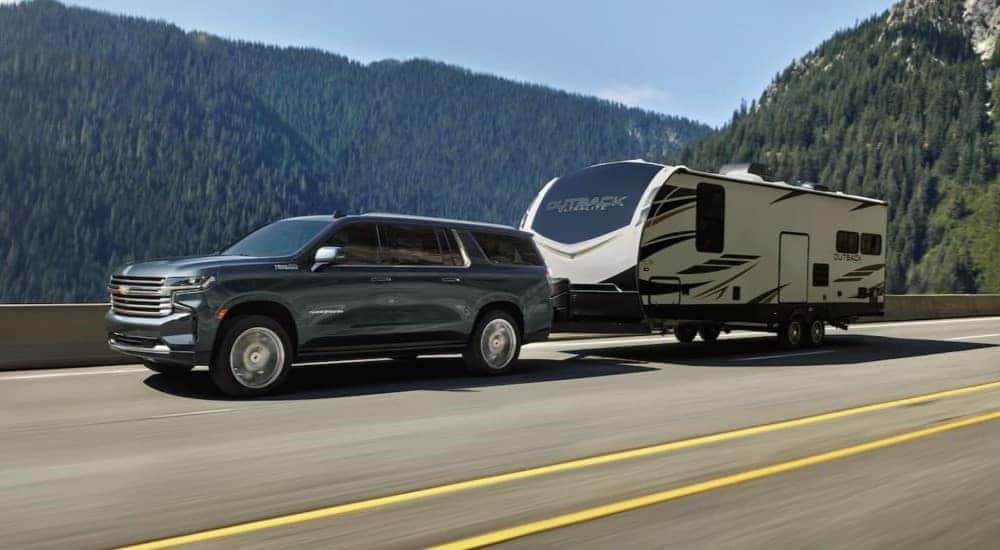 A gray 2021 Chevy Suburban High Country is shown towing a trailer on a highway.