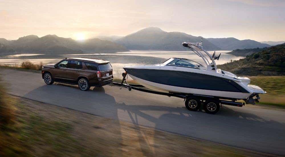A brown 2022 Chevy Tahoe is shown towing a boat near a lake.