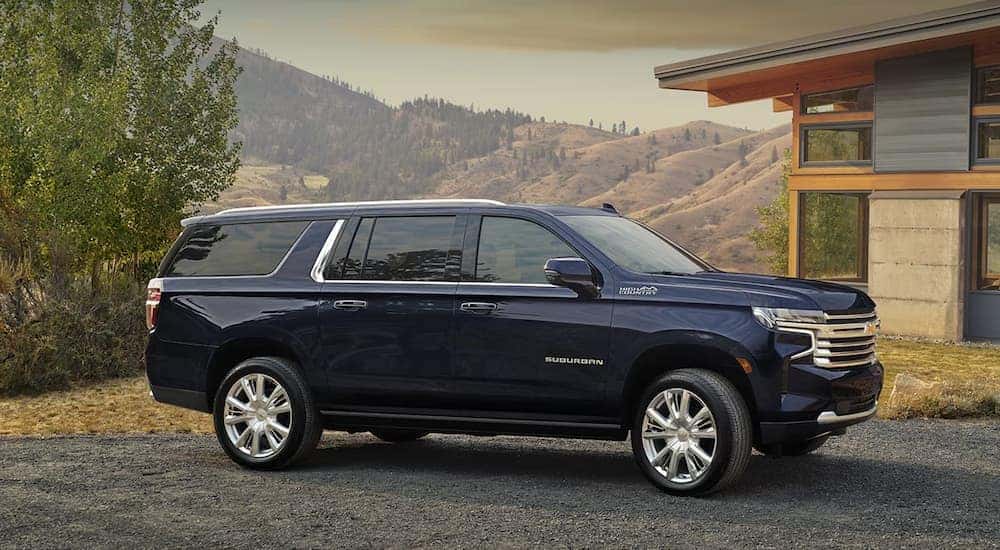 Side angle view of a blue 2025 Chevy Suburban High Country parked outside a building.
