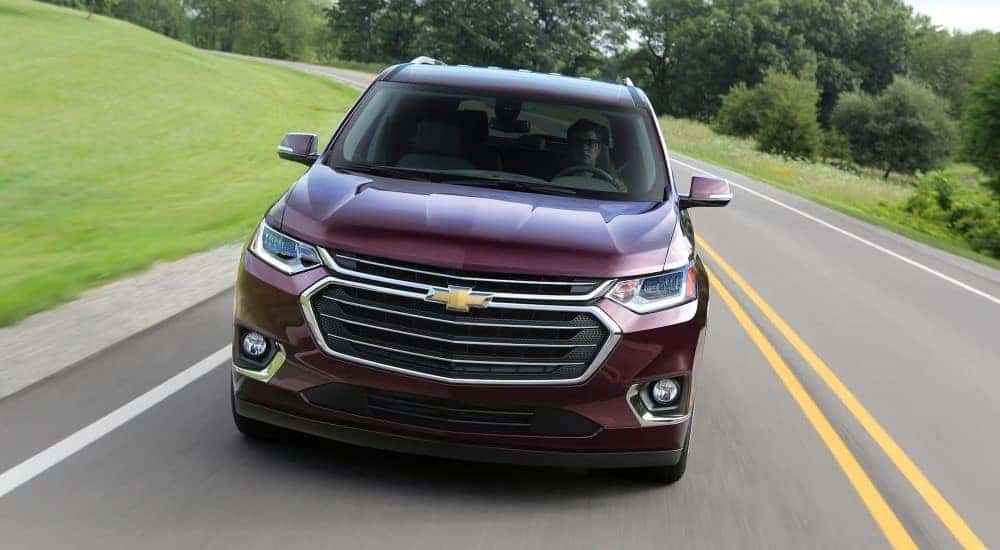 A burgundy 2018 Chevy Traverse for sale is shown driving on a highway.
