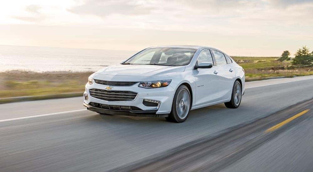 A white 2016 Chevy Malibu driving from a used car dealership near me.