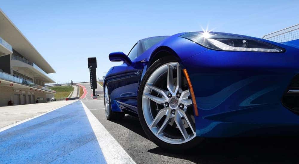 A close-up shows a silver wheel on a blue 2019 Chevy Corvette Stingray at a race track.