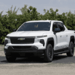 White Chevrolet Silverado EV parked outdoors on a sunny day with trees in the background, showcasing its modern front-end design and electric pickup styling.