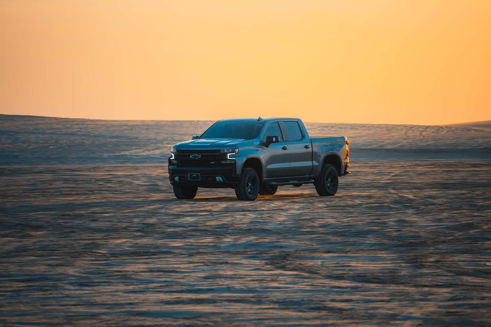 Chevrolet Silverado pickup truck driving across a sandy desert landscape at sunset, highlighting its rugged capability and off-road performance.