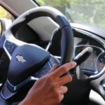 Close-up of a hand on the steering wheel of a Chevrolet car, showing dashboard and interior details on a sunny day