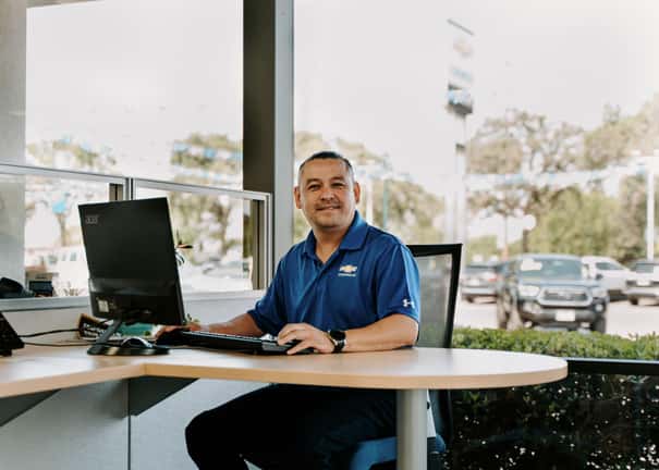 Man sitting inside a dealership, smiling while on his computer.