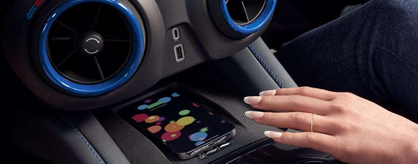 A person placing their phone on a wireless charging pad in the black interior of a 2024 Chevy Blazer.