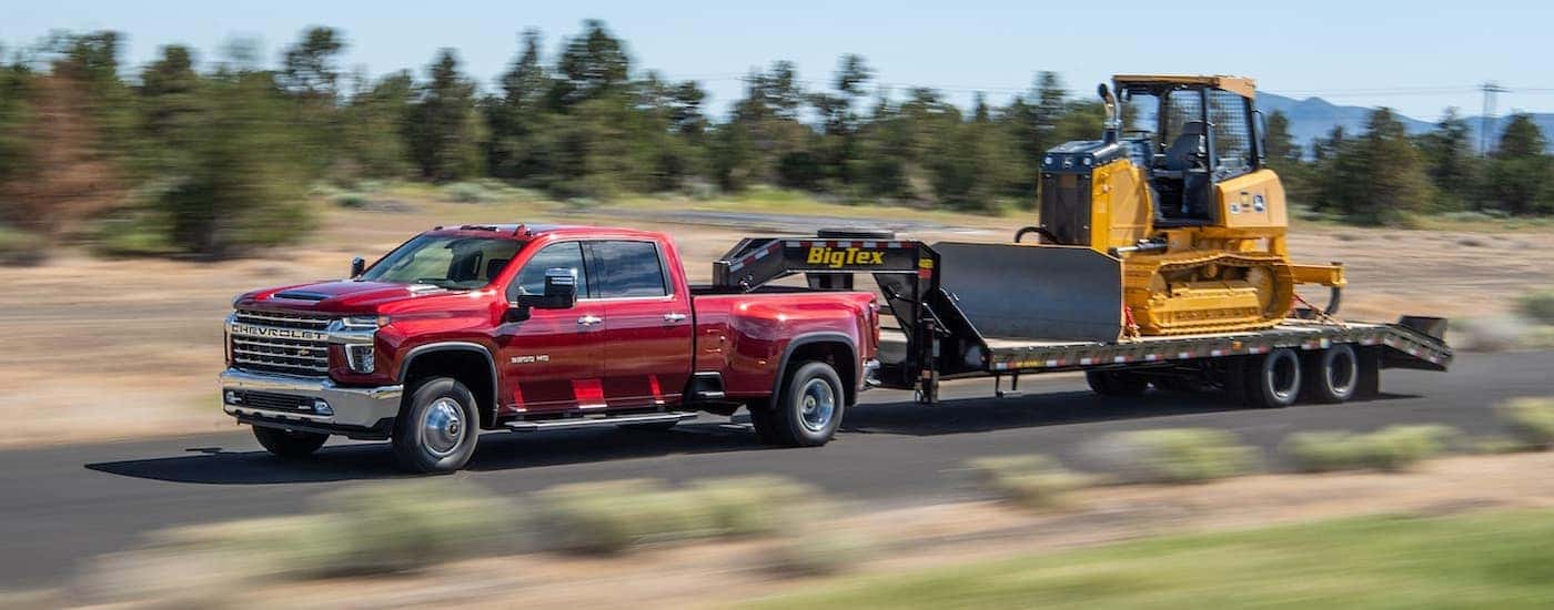 A red 2021 Chevy Silverado 3500 towing heavy machinery.