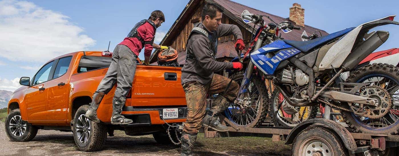 An orange 2022 Chevy Colorado Z71 is hooked up to a trailer with dirtbikes.