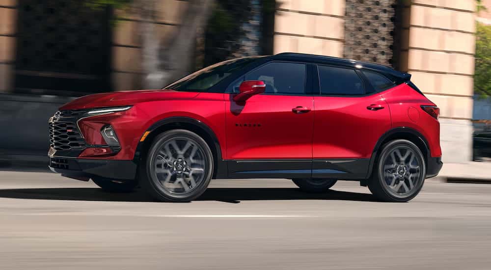 Side angle view of a red 2025 Chevy Blazer driving from a Chevy dealer near me.
