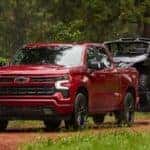 A red 2025 Chevy Silverado 1500 RST is shown towing a trailer.