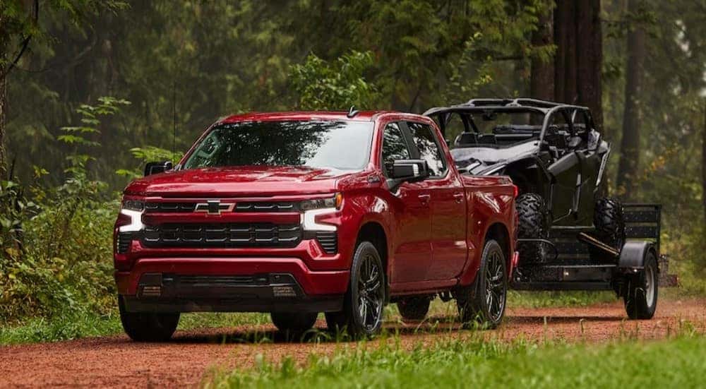 A red 2025 Chevy Silverado 1500 RST is shown towing a trailer.