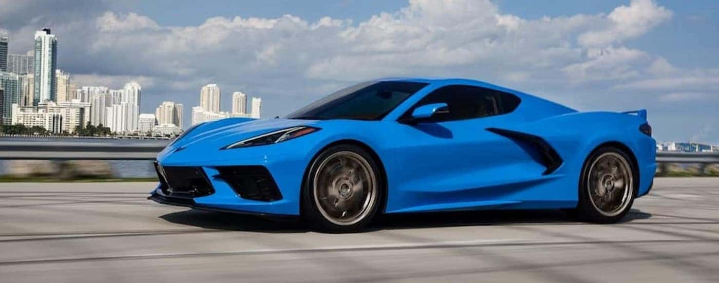A blue 2024 Chevy Corvette Stingray is shown driving near a city.