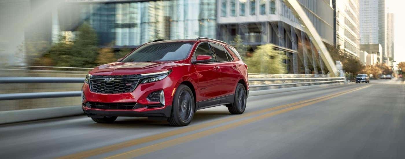 A red 2024 Chevy Equinox RS driving on a city street after visiting a used Chevy dealer