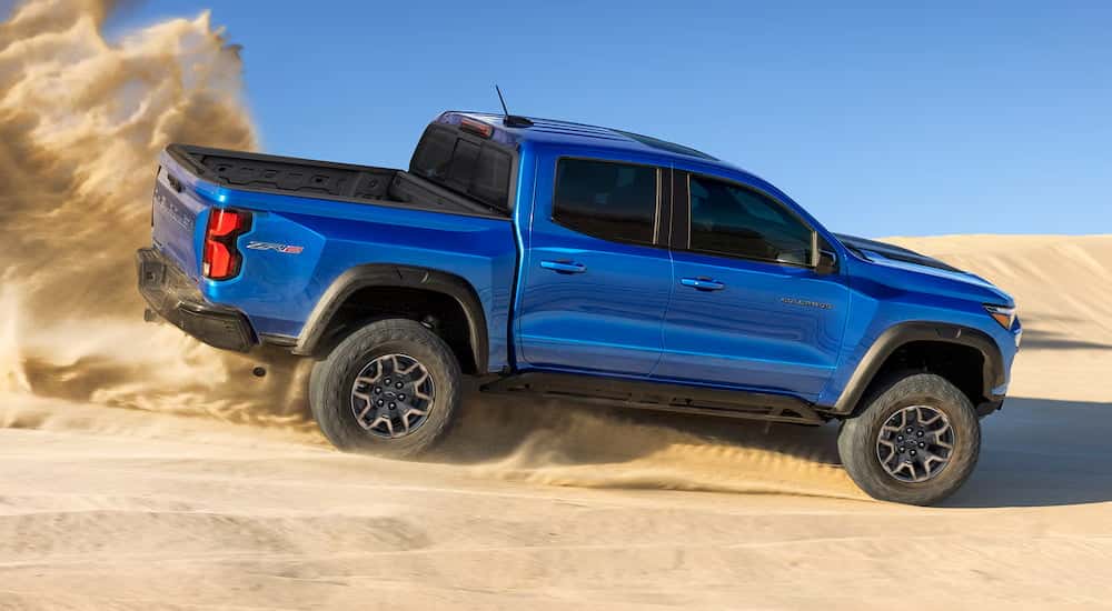 Rear of a blue 2026 Chevy Colorado driving off-road down a road.