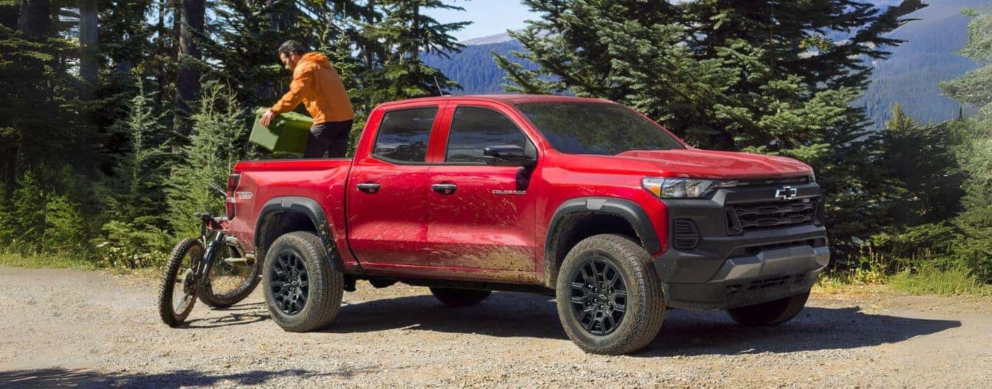A red 2023 Chevy Colorado parked at a trail with a person unloading a bike and cooler.