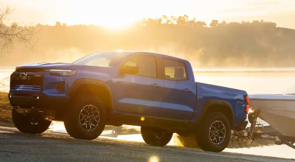 A side view of a blue 2026 Chevy Colorado towing a boat by sunset.