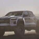 A white 2026 Chevy Colorado driving through a dust cloud.