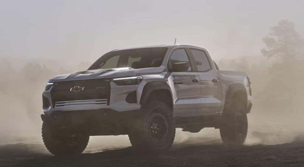 A white 2026 Chevy Colorado driving through a dust cloud.