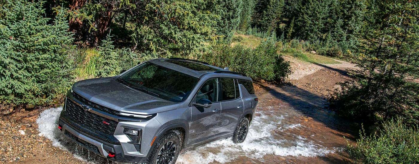 A silver 2026 Chevy Traverse off-roading in a stream